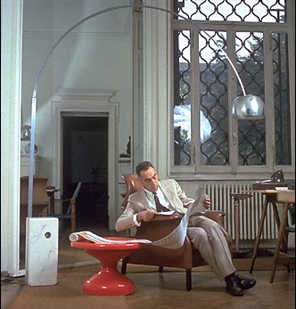 Achille Castiglioni in his studio, under an "Arco" lamp, sitting on "Sanluca" chair, next to a "Rochcetto" table.